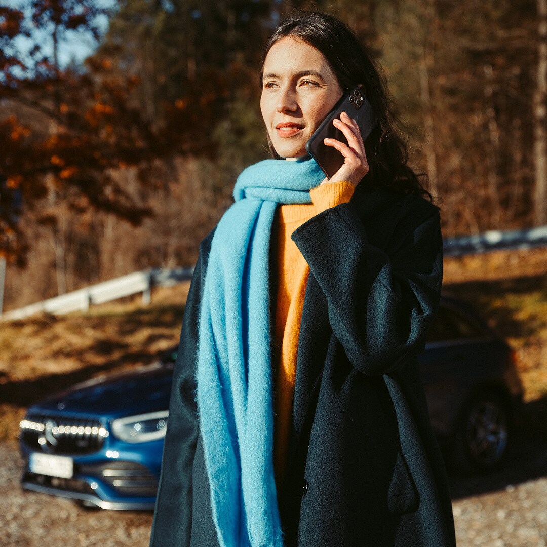 Hulp bij pech | Mercedes-Benz Een vrouw staat voor haar Mercedes SUV en telefoneert met een smartphone.