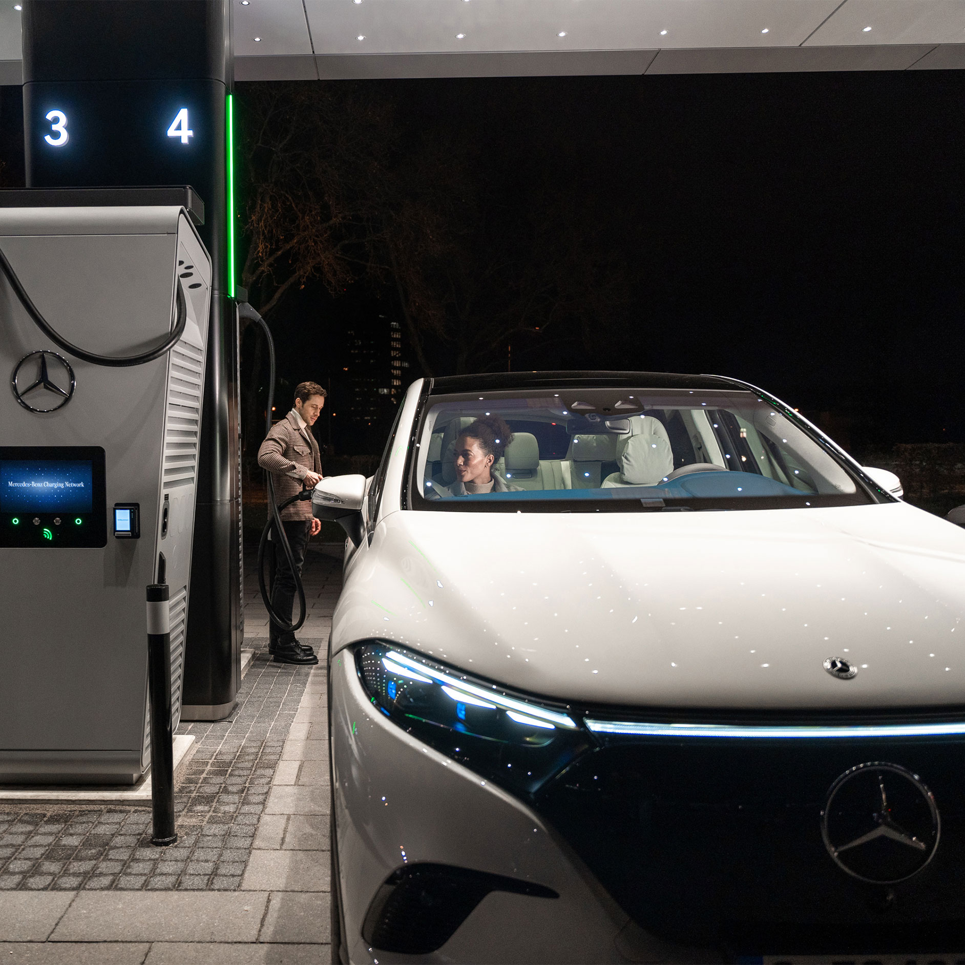 Opladen bij een publiek oplaadpunt | Opladen | Mercedes-Benz Een persoon laadt een Mercedes-Benz EQS SUV op bij een oplaadpunt.