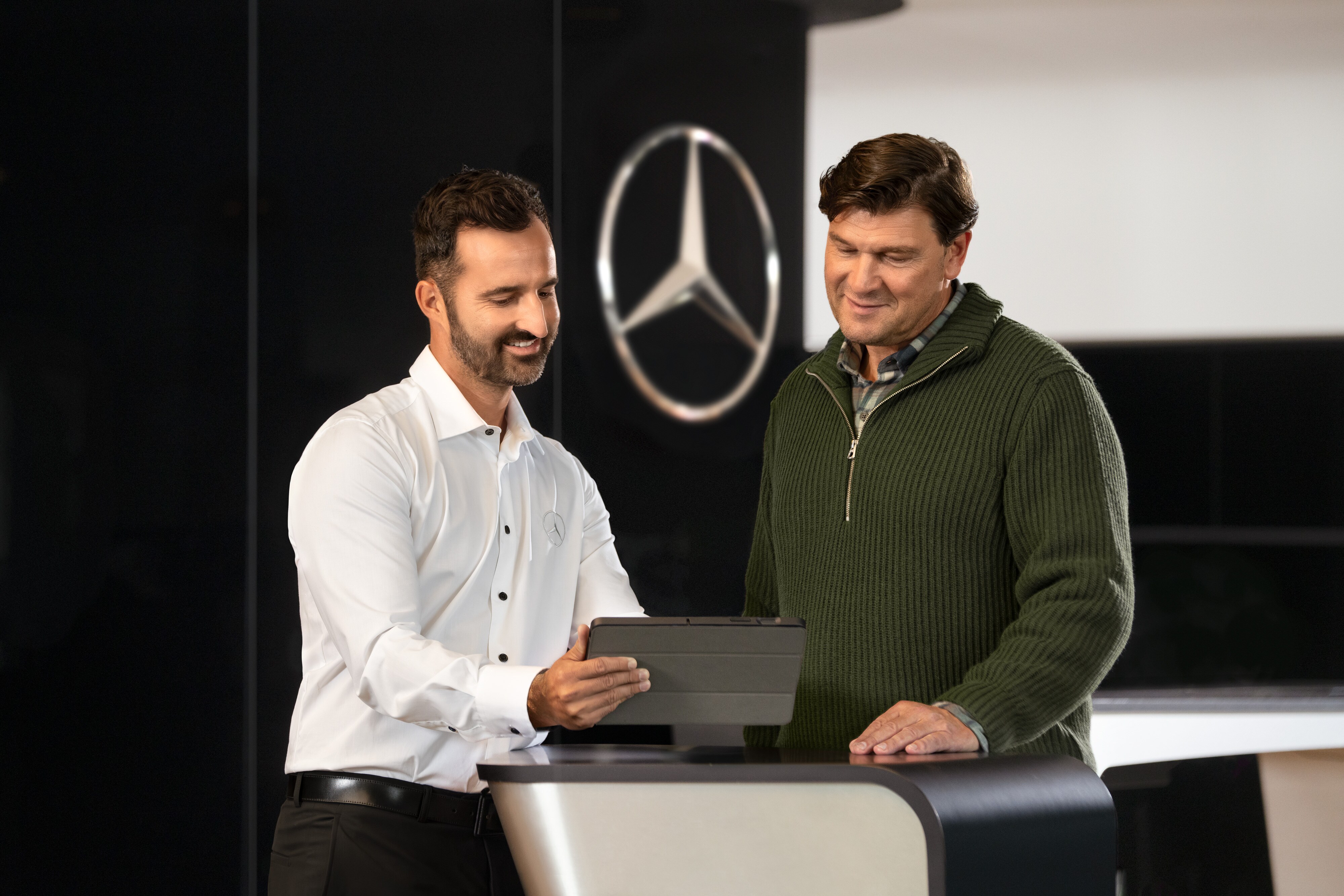 Mercedes-Benz Bedrijfswagens | Servicesoverzicht Twee mannen bespreken Mercedes-Benz bedrijfswagens aan een balie terwijl ze samen op een tablet kijken.