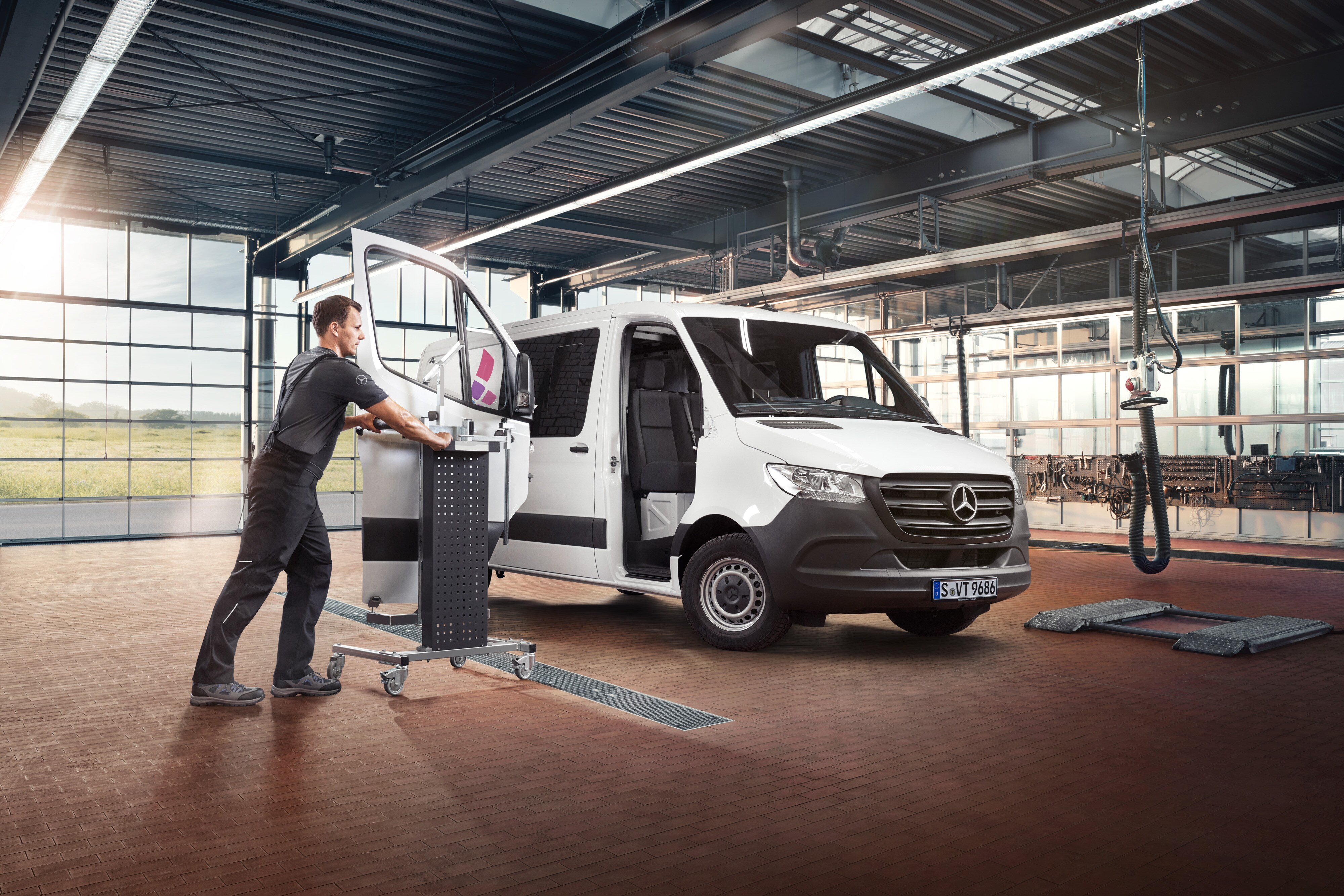 Mercedes-Benz Bedrijfswagens | Servicesoverzicht Reparatie Monteur repareert de passagiersdeur van een witte Mercedes-Benz Sprinter Gesloten Bestelwagen in de werkplaats.